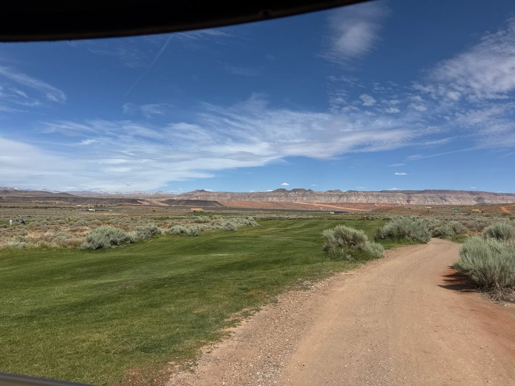 A dirt cart path through sagebrush and grass with red rock mesas on the horizon, southern Utah