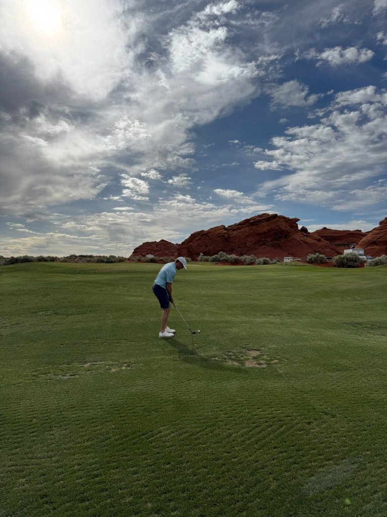 A golfer hitting from the fairway with red rock formations behind him at Sand Hollow, Hurricane, Utah